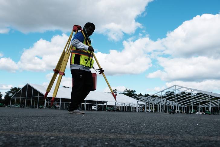A land surveyor walks by large tents being constructed in a parking lot at Orchard Beach in the Bronx on September 28th, 2022.